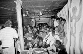 A crowded underground music venue with a diverse audience enjoying a performance, captured in black and white.
